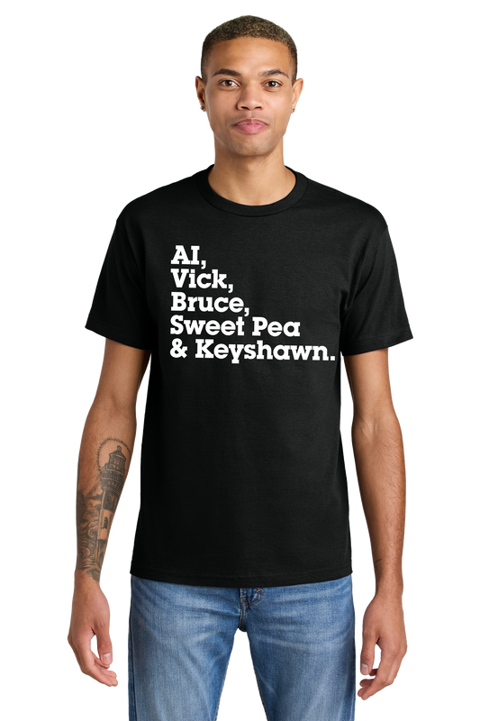 A man wearing a black t-shirt featuring bold white text that reads "AI, Vick, Bruce, Sweet Pea & Keyshawn." The shirt pays tribute to legendary athletes from Norfolk, including Allen Iverson, Michael Vick, Bruce Smith, Pernell "Sweet Pea" Whitaker, and Keyshawn Davis.