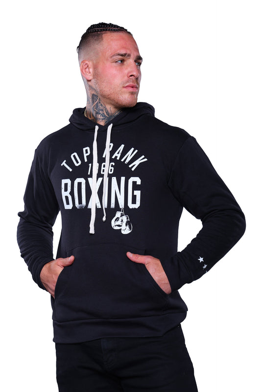 Person wearing a black pullover hoodie with "Top Rank Boxing 1966" printed in white on the front and three stars on the left sleeve, paired with black pants.